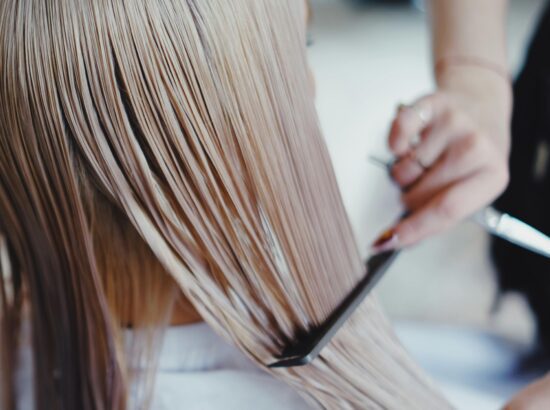 Close-up of a hairstylist arranging long, straight blonde hair in a salon environment.