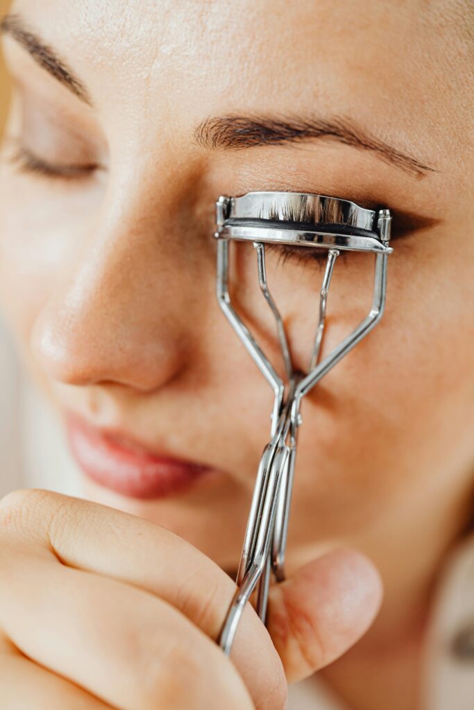 A woman gently curls her eyelashes with a metal eyelash curler.