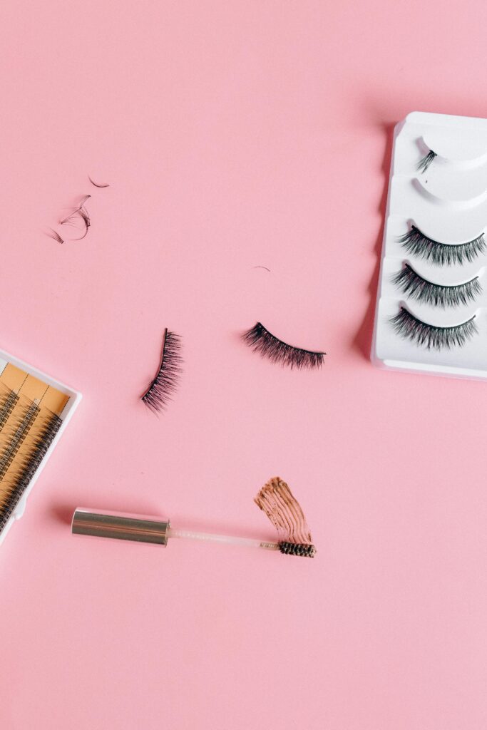 Collection of false eyelashes and tools on a pink surface ideal for beauty product promotion.