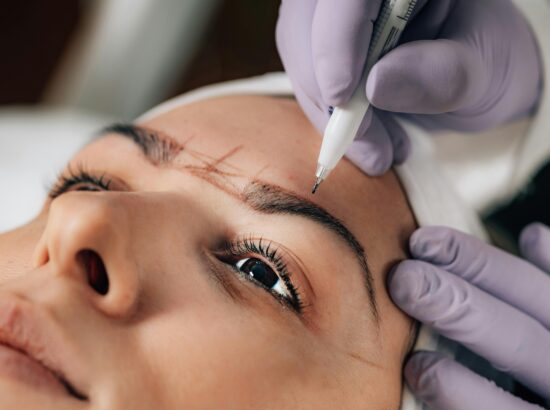 A beautician performs precise microblading on a client's eyebrows in a salon.